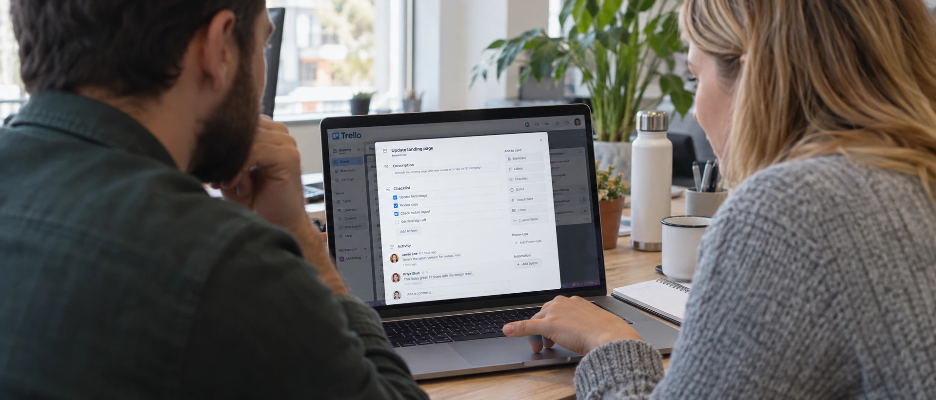 Two colleagues reviewing a shared Trello board on a laptop.